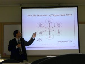 Paul Trafford giving a presentation, pointing to a projector screen that is displaying 6 directions (indicated as N, E, S, W, up and down) with a man in the middle connected to different kinds of people